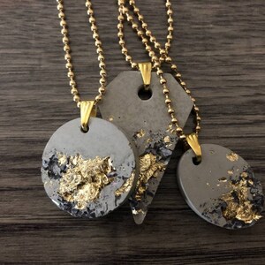 May include: Three necklaces with gold chains and gray concrete pendants with gold leaf accents. The pendants are in the shapes of a circle and a triangle.
