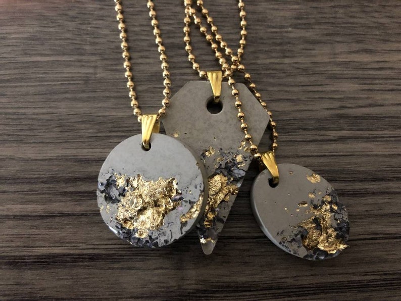 May include: Three necklaces with gold chains and gray concrete pendants with gold leaf accents. The pendants are in the shapes of a circle and a triangle.