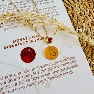 Può includere: Collana dorata con ciondolo con il segno zodiacale Leone. La collana ha una piccola gemma rossa ed è esposta su una carta con testo in tedesco e l'immagine di un rubino.