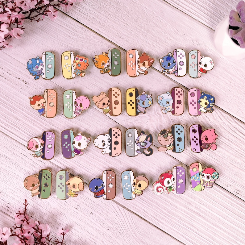 May include: A set of 18 enamel pins featuring various animal characters from the Animal Crossing video game series. Each pin depicts a different character holding a Nintendo Switch controller. The pins are colorful and have a glossy finish.