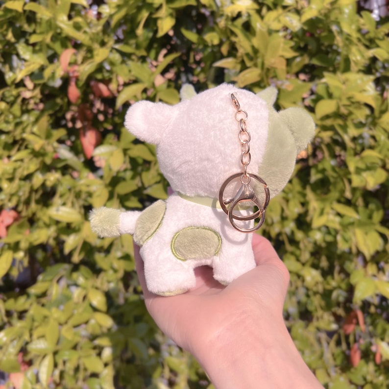 May include: White plush cow keychain with green spots and a gold chain and key ring.