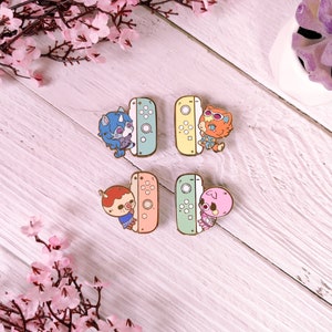 May include: Four enamel pins featuring characters from the Animal Crossing video game series. Each pin features a different character holding a Nintendo Switch console. The characters are a blue and purple unicorn, a red fox, a pink pig, and a brown bear. The pins are all different colors, with a light blue, yellow, green, and orange background.