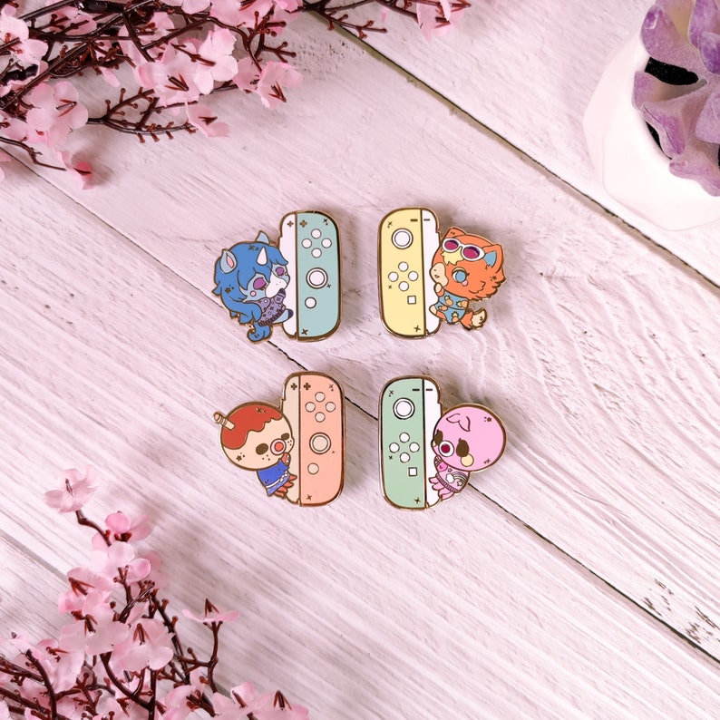 May include: Four enamel pins featuring characters from the Animal Crossing video game series. Each pin features a different character holding a Nintendo Switch console. The characters are a blue and purple unicorn, a red fox, a pink pig, and a brown bear. The pins are all different colors, with a light blue, yellow, green, and orange background.