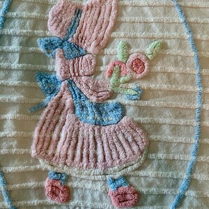 May include: A vintage, white, crocheted throw blanket with a pink and blue embroidered design of a little girl holding a flower.