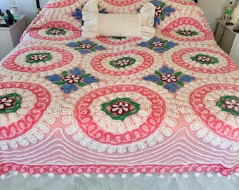May include: A pink and white crocheted bedspread with a floral pattern. The bedspread has a white ruffled edge and a white tulle bed skirt.