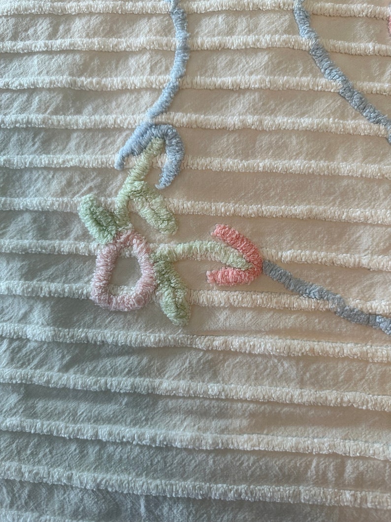 May include: A close-up of a white fabric with a raised, embroidered design. The design features a light blue, pink, and green floral pattern.