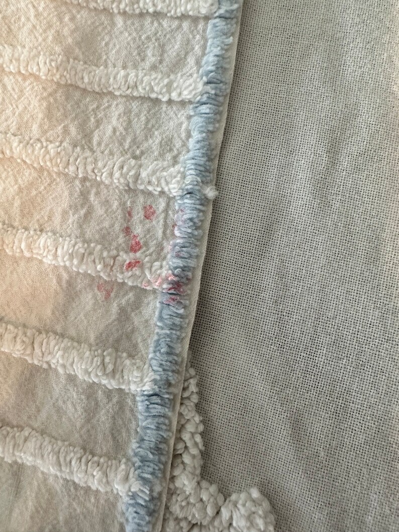 May include: Close-up of a white textured fabric with a blue trim. The fabric has a few small pink stains.