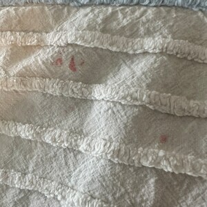 May include: Close-up of a white fabric with a textured, fluffy design. There are two small pink stains on the fabric.