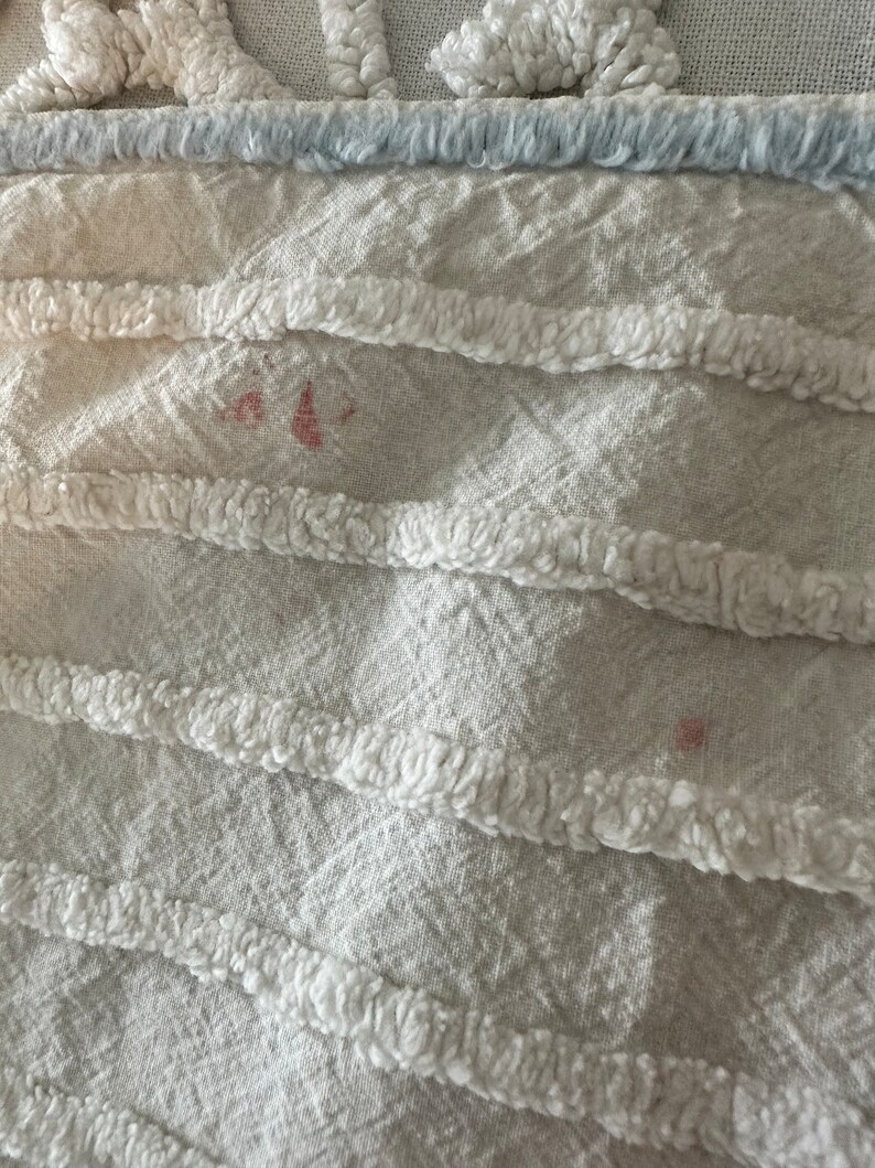 May include: Close-up of a white fabric with a textured, fluffy design. There are two small pink stains on the fabric.