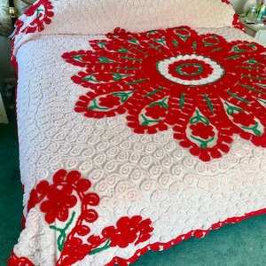 May include: A white and red vintage chenille bedspread with a large red and green floral design. The bedspread has a scalloped edge.