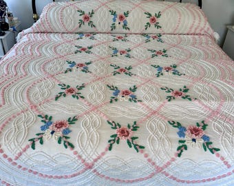 May include: A white chenille bedspread featuring a raised lattice pattern with pink tufted accents and embroidered floral clusters in pink, blue, and green. The bedspread has a scalloped edge with a long white fringe along the bottom border.