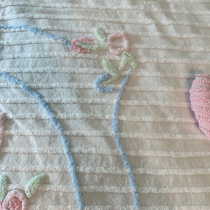 May include: White cotton bedspread with a blue and pink floral design. The design is embroidered and raised. The bedspread has a striped texture.