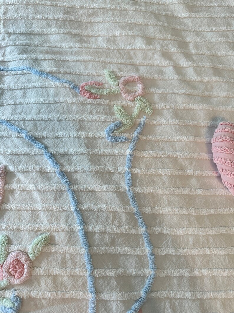 May include: White cotton bedspread with a blue and pink floral design. The design is embroidered and raised. The bedspread has a striped texture.