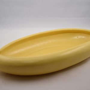 May include: A yellow ceramic banana-shaped serving dish. The dish is smooth and glossy.