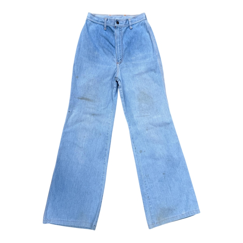 K&ouml;nnte beinhalten: Hellblaue Jeanshose mit hoher Taille und ausgestellten Beinen. Die Hose hat einen Knopf- und Rei&szlig;verschluss und weist einige Verf&auml;rbungen auf. Ein klassischer Vintage-Stil.