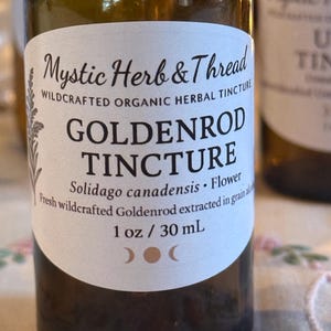 Puede incluir: Una botella de vidrio marrón con una etiqueta blanca que dice "Mystic Herb & Thread" y "Goldenrod Tincture". La etiqueta también incluye "1 oz / 30 ml" e información botánica. La botella contiene líquido.