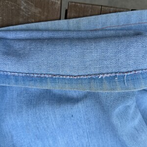K&ouml;nnte beinhalten: Nahaufnahme einer hellblauen Jeans, mit hochgekrempeltem Saum. Der Saum ist sichtbar und zeigt die N&auml;hte und leichte Abnutzung. Der Denim hat ein verwaschenes Aussehen.