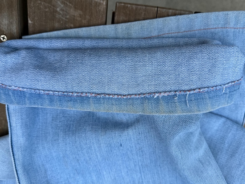 K&ouml;nnte beinhalten: Nahaufnahme einer hellblauen Jeans, mit hochgekrempeltem Saum. Der Saum ist sichtbar und zeigt die N&auml;hte und leichte Abnutzung. Der Denim hat ein verwaschenes Aussehen.