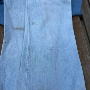 K&ouml;nnte beinhalten: Hellblaue Jeanshose mit sichtbaren Flecken und Abnutzungserscheinungen. Die Hose ist gefaltet und zeigt die Vorder- und Seitenn&auml;hte. Der Denim hat ein verwaschenes Aussehen, was auf Alter oder Waschen hindeutet. Wahrscheinlich Vintage oder gebraucht.