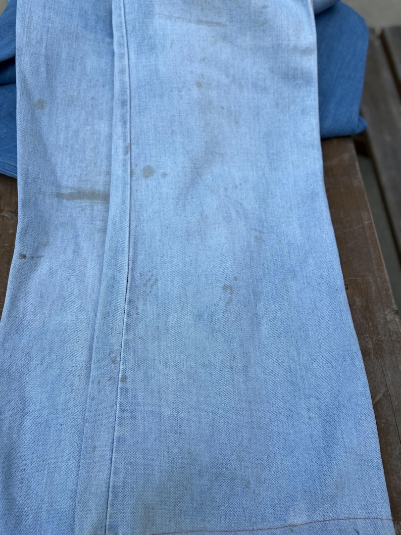 K&ouml;nnte beinhalten: Hellblaue Jeanshose mit sichtbaren Flecken und Abnutzungserscheinungen. Die Hose ist gefaltet und zeigt die Vorder- und Seitenn&auml;hte. Der Denim hat ein verwaschenes Aussehen, was auf Alter oder Waschen hindeutet. Wahrscheinlich Vintage oder gebraucht.