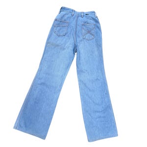 K&ouml;nnte beinhalten: Hellblaue Jeans mit hoher Taille und weitem Bein. Die R&uuml;ckseite hat zwei Taschen und eine dekorative X-Naht. Die Jeans sind aus hellem Denim-Material.