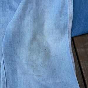 K&ouml;nnte beinhalten: Nahaufnahme von hellblauem Denim-Stoff mit sichtbarer Textur und leichter Verf&auml;rbung. Das Bild zeigt einen Abschnitt aus Denim, m&ouml;glicherweise von Jeans oder einer Jacke, mit einer Naht und Nahtdetails.