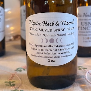 May include: A brown glass bottle with a white label featuring the text "Mystic Herb & Thread IONIC SILVER SPRAY 30 ppm." The label also includes the text "Wildcrafted Spiritual Natural Healing." The bottle contains 2 oz of liquid.