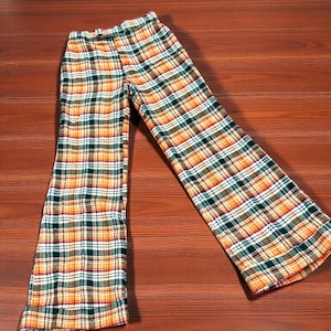 May include: A pair of plaid pants in a warm color palette of orange, green, white, and brown. The pants have a wide-leg design and a button closure at the waist. The plaid pattern is evenly distributed across the fabric.