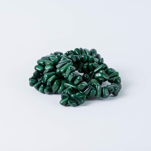 May include: A dark green beaded bracelet composed of polished, irregularly shaped stones. The bracelet is coiled on a white surface, showcasing the glossy texture and rich color of the gemstones. The beads are approximately 0.5 inches in length.