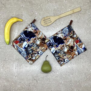 May include: Two square quilted pot holders with a cat print. The holders feature various cat breeds in shades of brown, grey, and white. A wooden spoon, a yellow banana, and a green pear are also present.
