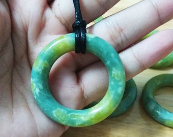 May include: A green and yellow jade ring pendant with a black cord necklace. The ring is smooth and polished with a marbled pattern.