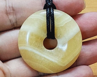 May include: A yellow and white donut-shaped pendant with a black cord. The pendant has a smooth, polished surface and a hole in the center. #A1