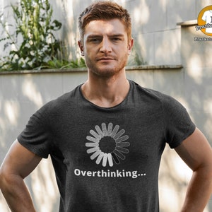 May include: Dark gray t-shirt with a white graphic of a loading circle and the word "Overthinking..." printed below. The shirt is a crew neck style and is being worn by a person.