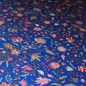 May include: Close-up of a blue fabric with a floral pattern. The design features pink, red, and white flowers with green leaves and stems. The background is a deep blue color, creating a vibrant and detailed textile.