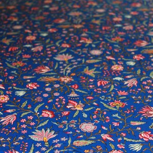 May include: Close-up of a vibrant blue fabric with a repeating floral pattern. The design features pink, red, and green flowers with delicate leaves and stems. The fabric is likely used for textiles or home decor.