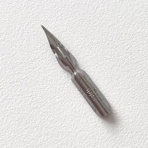 May include: A close-up of a silver pen nib with a sharp, pointed tip. The nib is made of metal and has a small, curved design. The nib is angled slightly to the right, against a textured white background.
