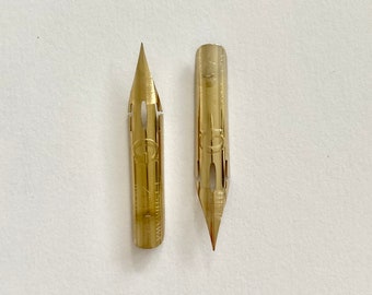 Könnte beinhalten: Zwei goldfarbene Kalligraphie-Federn mit einer spitzen Spitze. Die Federn sind für die Verwendung mit einem Federhalter gedacht.