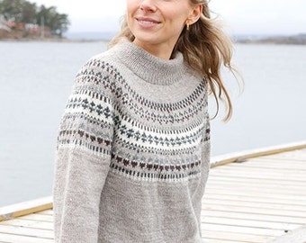 Puede incluir: Un suéter gris claro con cuello alto y canesú estampado. El canesú presenta un diseño repetitivo en blanco, gris y marrón. El suéter está hecho de un material de punto suave y lo lleva una persona.