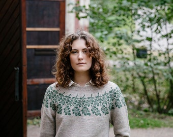 Könnte beinhalten: Hellbeige Strickpullover mit grünem Blattmuster auf Brust und Bündchen. Der langärmlige Pullover wird über einem weißen Hemd mit Kragen getragen. Das Kleidungsstück ist aus Strickmaterial.