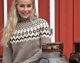 May include: A woman wearing a tan sweater with a geometric pattern in white and brown. The sweater has a high neckline. The background includes a red wooden wall and a rusty metal container.