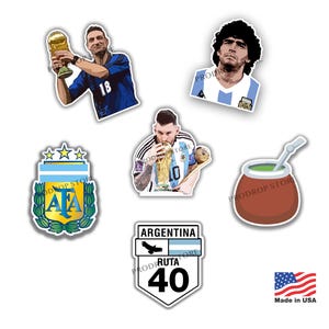 Puede incluir: Una colección de pegatinas con jugadores de fútbol argentinos, el logotipo de la selección argentina, una señal de tráfico y una taza de mate tradicional. Las pegatinas tienen varias formas y tamaños, con colores vibrantes e ilustraciones detalladas.