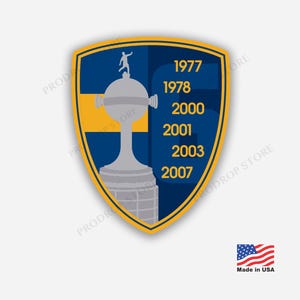May include: A shield-shaped sticker featuring a blue and yellow background with a grey trophy illustration. The trophy is topped by a small figure. The years 1977, 1978, 2000, 2001, 2003, and 2007 are printed in yellow on the right side of the shield.