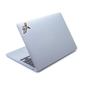 May include: A silver laptop computer with a sticker of a soccer player making a heart shape with his hands.