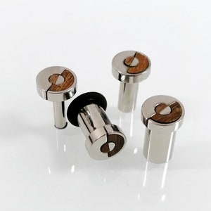 May include: Four silver-toned ear gauges with a wood inlay design. One gauge has a black rubber o-ring. The gauges are on a white background. The wood inlay is a light brown color.