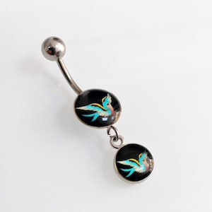 May include: A silver belly button ring with two dangling charms. Each charm is a black circle with a blue and yellow bird design.