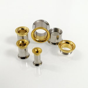 Peut inclure: Un ensemble de six jauges d'oreille en acier inoxydable avec des accents dorés. Les jauges sont de tailles différentes et sont disposées sur une surface blanche.