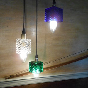 May include: Three pendant lights with different coloured glass shades. The shades are a clear glass with a diamond pattern, a blue glass with a diamond pattern, and a green glass with a diamond pattern.