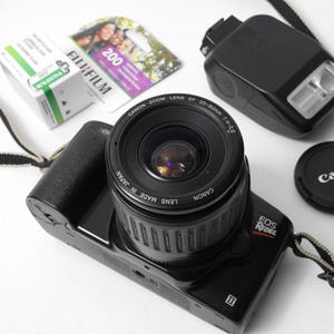 May include: A black Canon EOS Rebel camera with a Canon EF 35-80mm 1:4-5.8 zoom lens attached. The camera has a black strap and a Canon flash unit is attached to the hot shoe.
