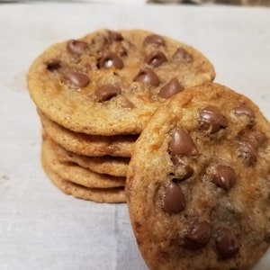 May include: A stack of freshly baked chocolate chip cookies. The cookies are golden brown and have a soft, chewy texture. The chocolate chips are melted and gooey.