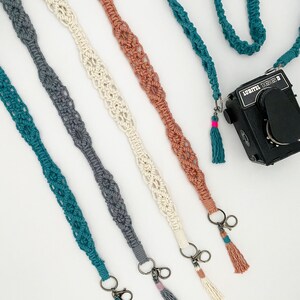 Puede incluir: Cinco correas de cámara de ganchillo en diferentes colores: azul verdoso, gris, blanco, beige y melocotón. Cada correa tiene un pequeño cierre de metal y un borla en el extremo.